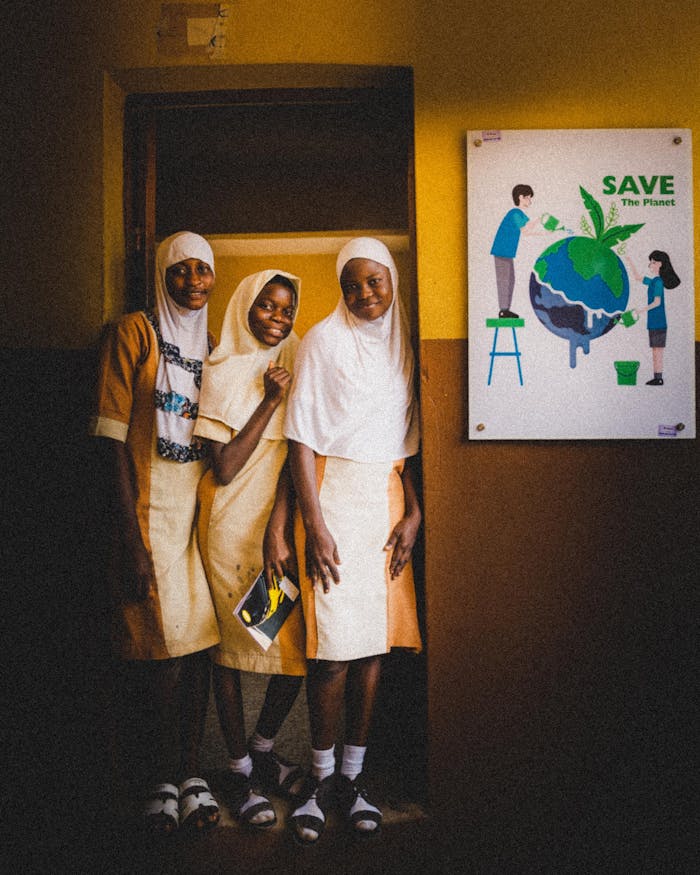 services-02 Three schoolgirls in uniform pose beside an environmental poster indoors.