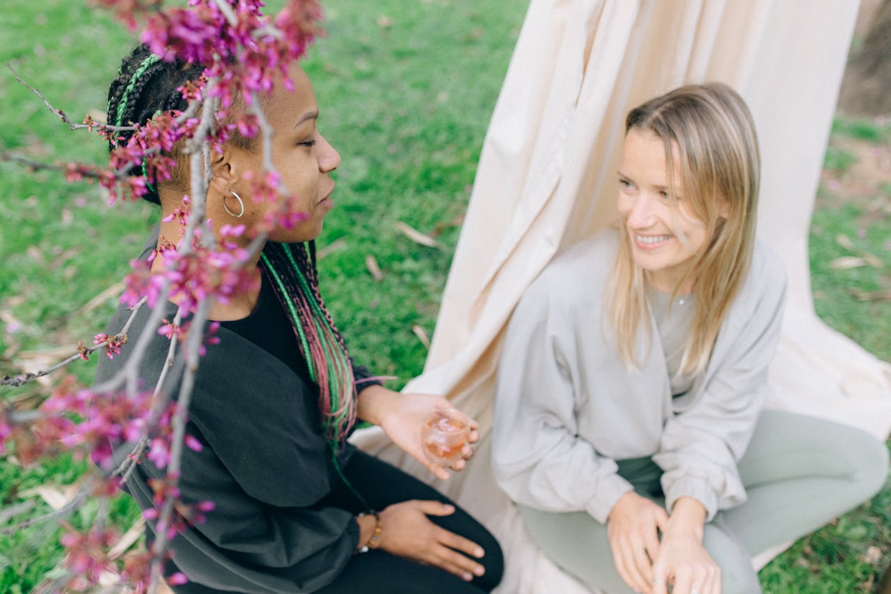 gallery-1 Two women enjoying a serene outdoor moment surrounded by spring blossoms.